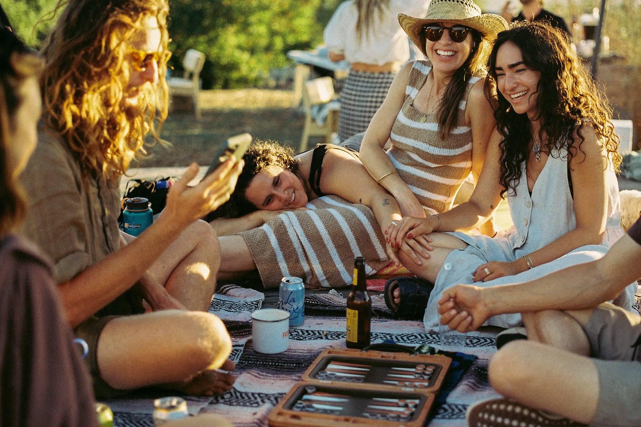 A group of friends sitting on a blanket  playing a game of backgammon on their Heirloom Board. 